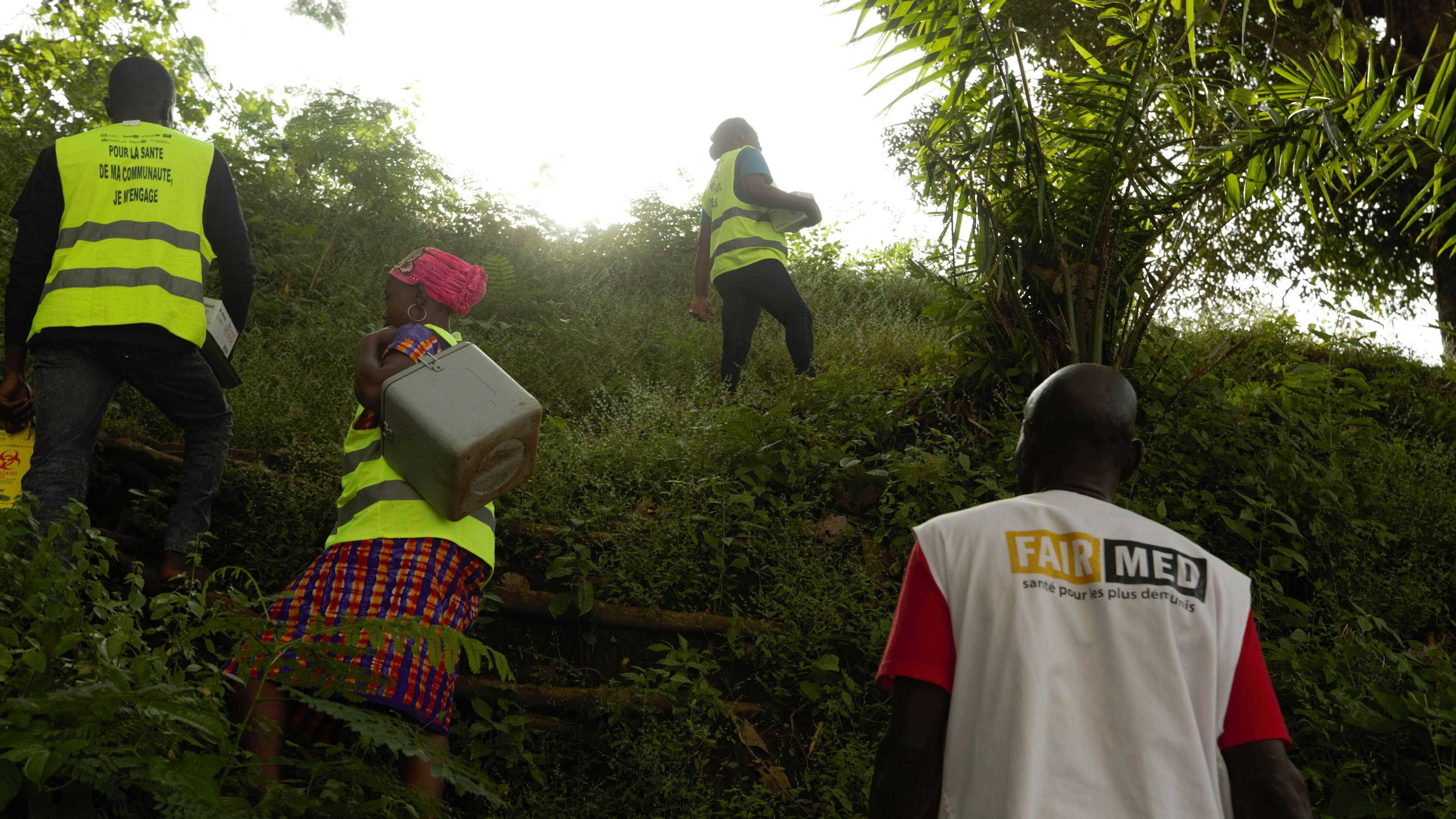 Auf dem Bild sieht man vier FAIRMED-Mitarbeitende, die die Impfstoffe durch den Wald tragen.